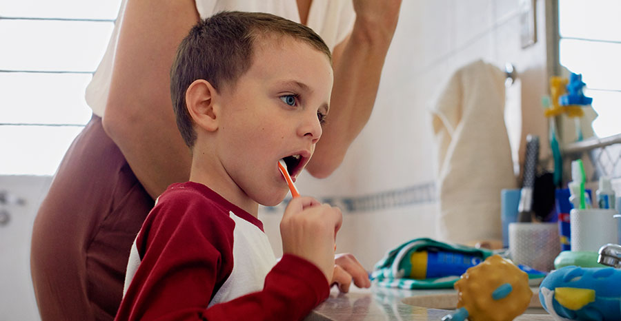 Child brshing teeth with parent in the background